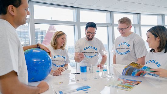 Ecolab associates in volunteer t-shirts conducting a small experiment on a tabletop.