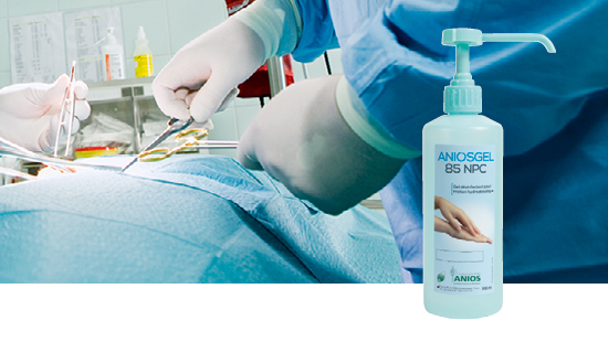 Surgical scene with medical professionals performing an operation and a bottle of ANIOSGEL 85 NPC hand sanitizer in the foreground.
