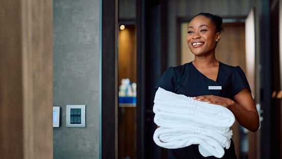 Housekeeping staff member holding folded towels in a hotel room doorway.